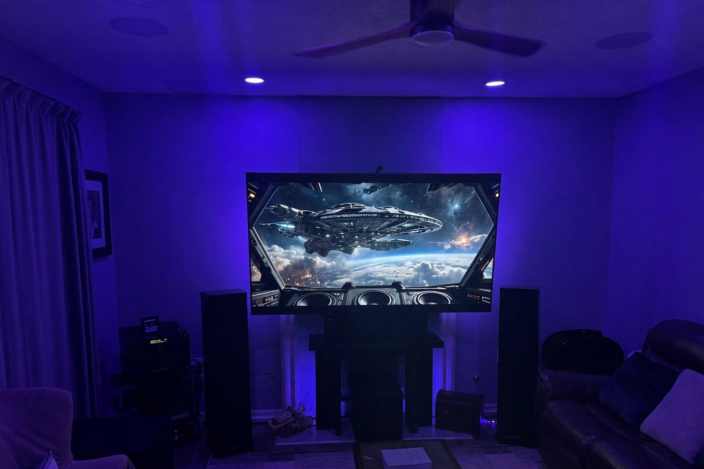 A living room home theater lit in blue and violet, with tower speakers on either side of a large screen