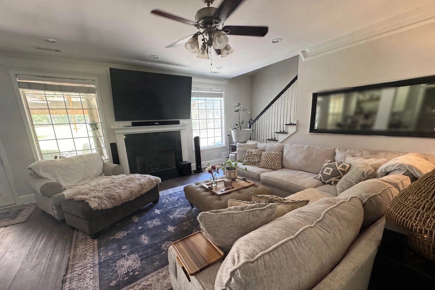 A living room in daylight with a wall-mounted TV, a soundbar on the mantel, tower speakers and a sectional sofa